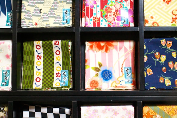 Various squares of colorful fabric are neatly displayed in a black grid. Each fabric features a unique pattern, including floral designs, geometric shapes, and prints with small owl illustrations. The colors range from vibrant reds and blues to muted greens and yellows.