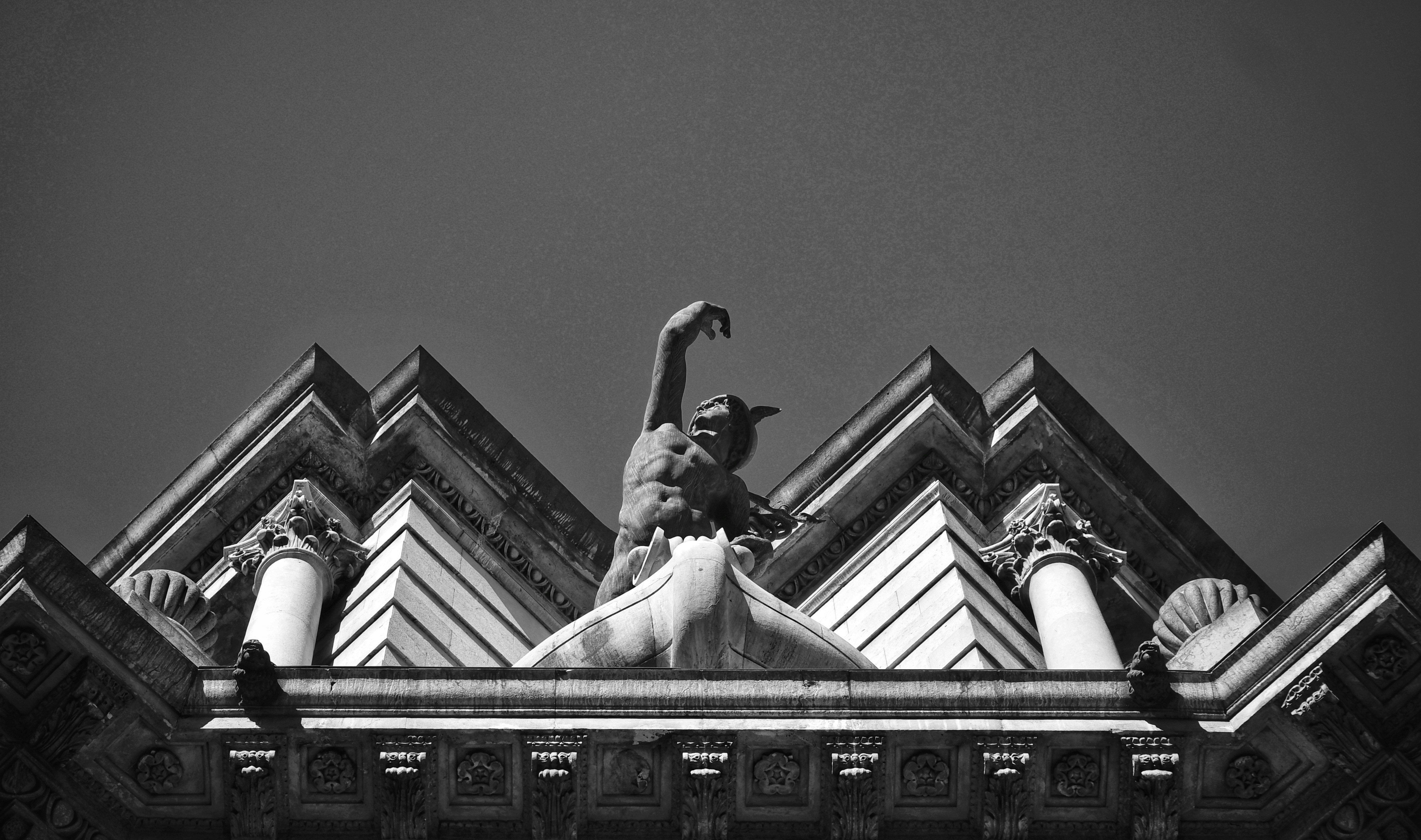 Centered in this black and white photo is a statue of Mercury on the corner of an old building.
