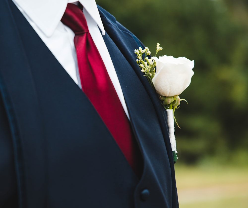 Un uomo in giacca e cravatta con una cravatta rossa e una rosa bianca in grembo