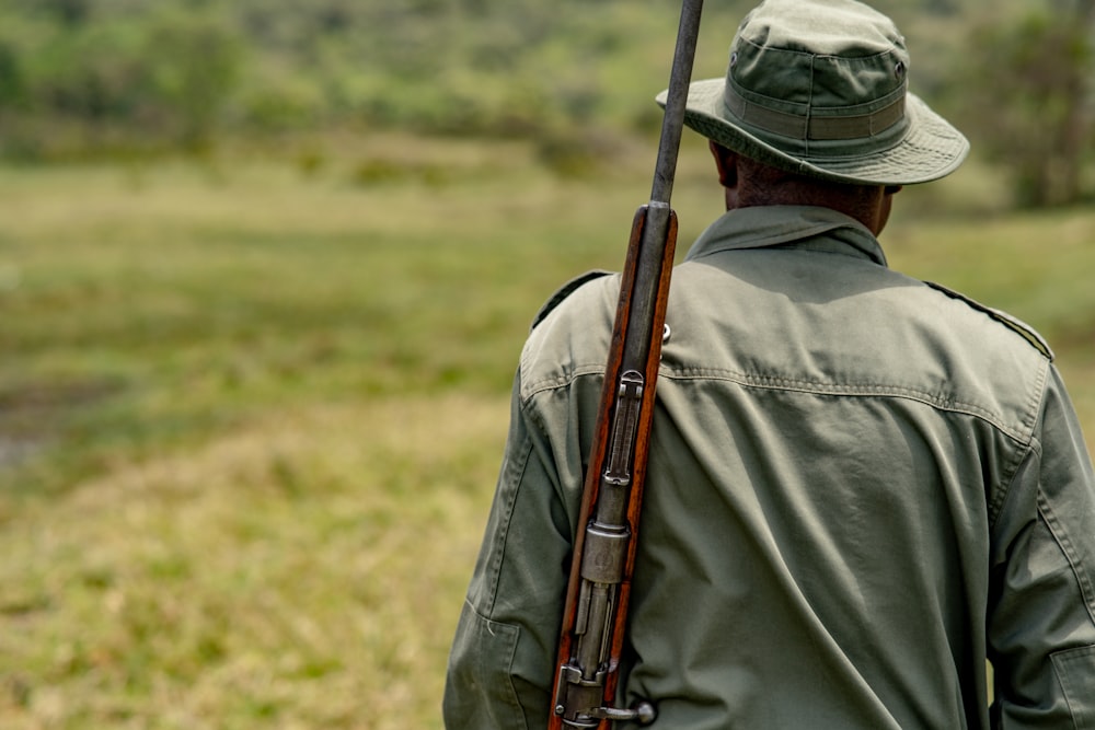 um homem segurando um rifle enquanto está em pé em um campo