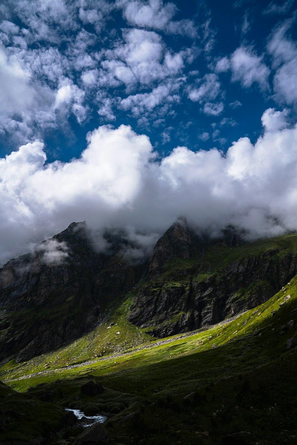 a mountain with a stream running through it under a cloudy sky