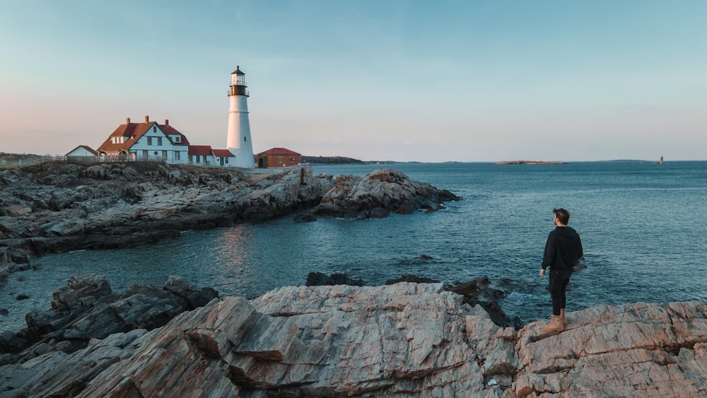 a man standing on a rock next to a lighthouse
