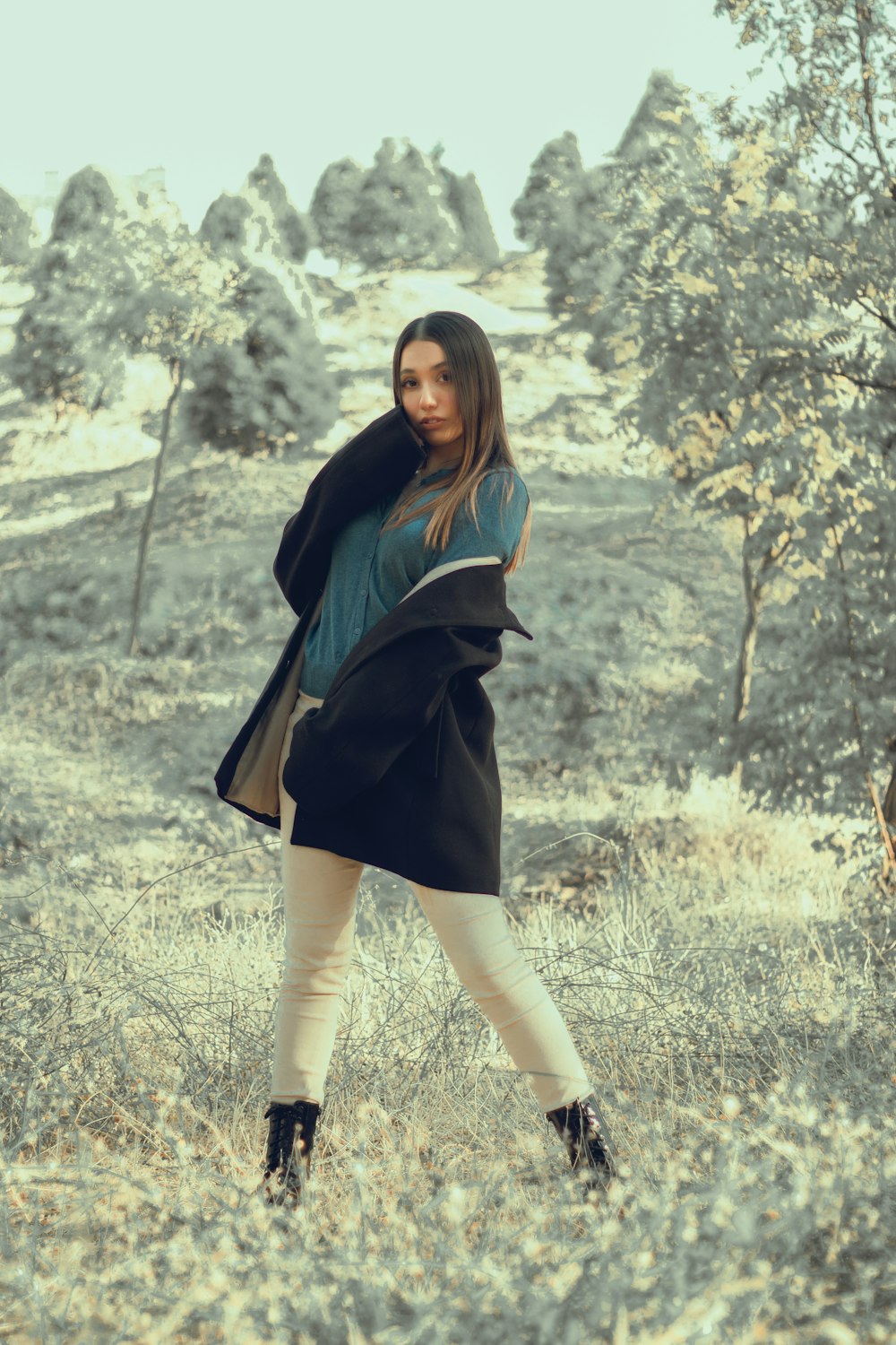 a woman standing in a field with trees in the background