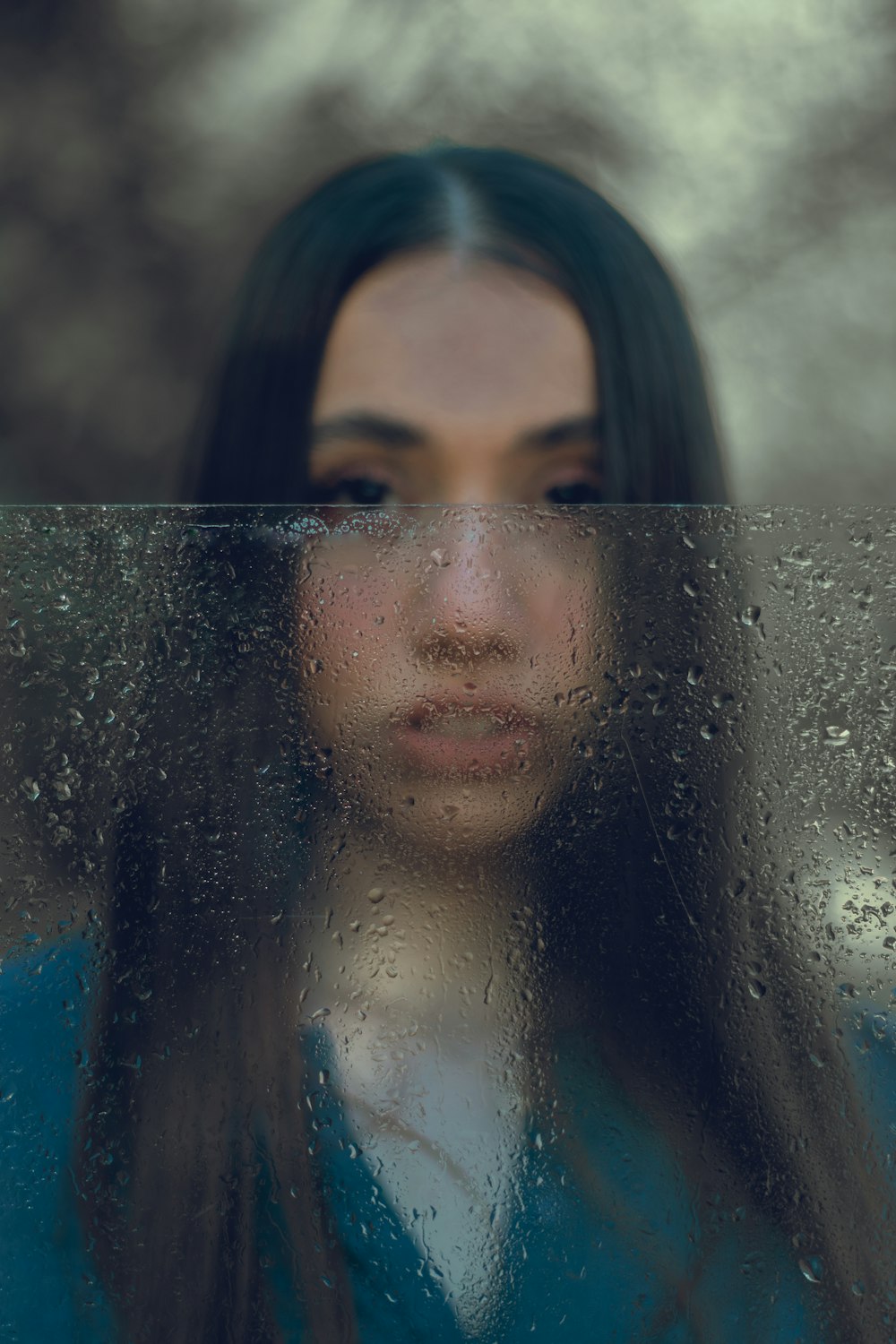 uma mulher olhando através de uma janela coberta de chuva