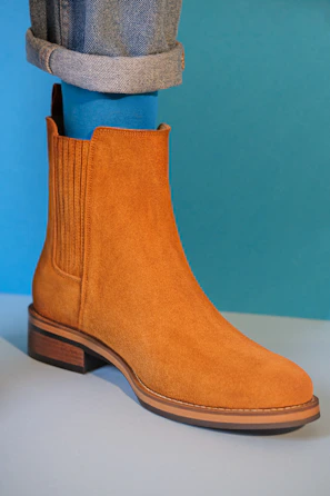 Trendy ankle boots in neutral colors styled with denim jeans against a bright, colorful backdrop.