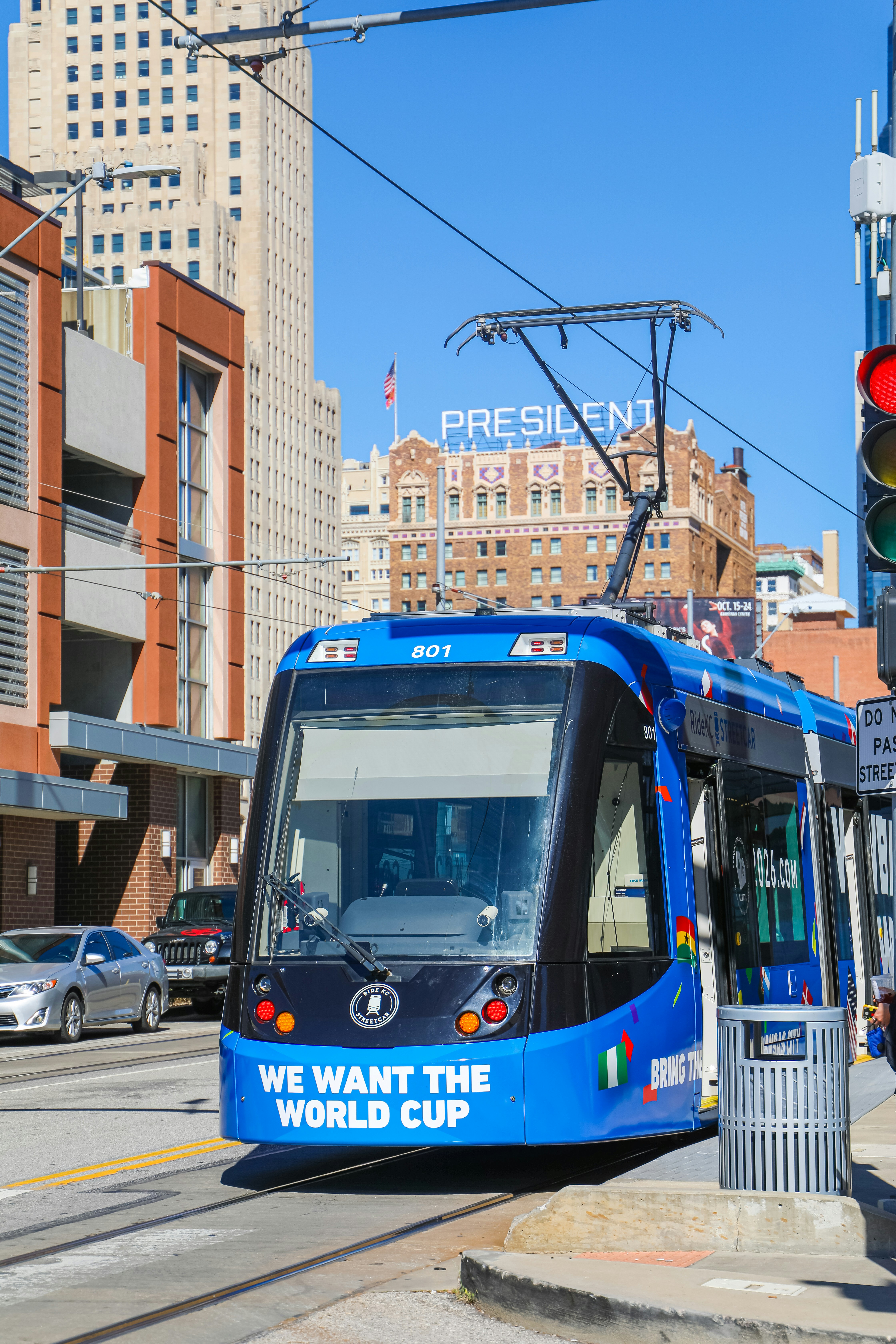 a blue train traveling down a street next to tall buildings