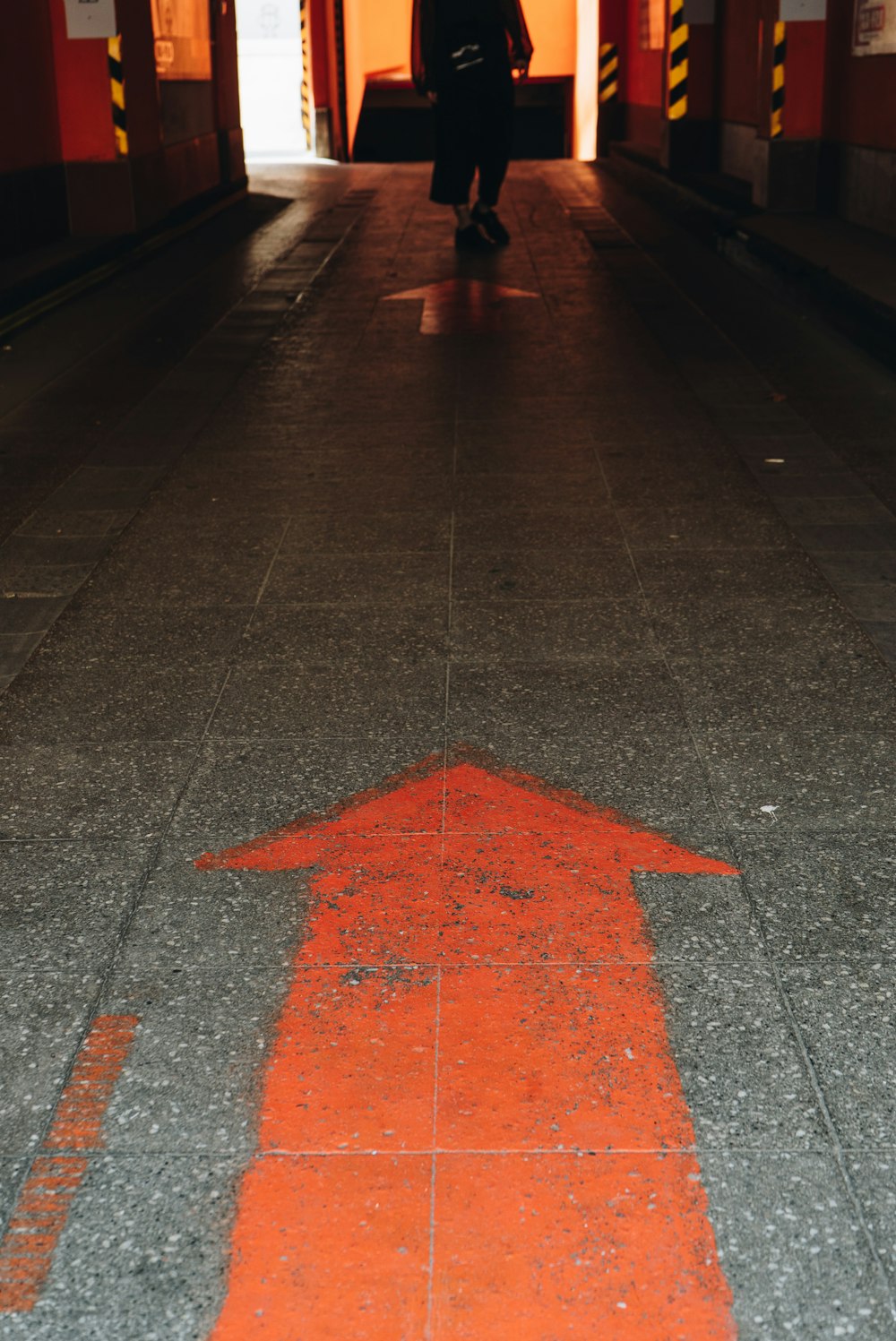 a person walking down a hallway with an arrow painted on the floor