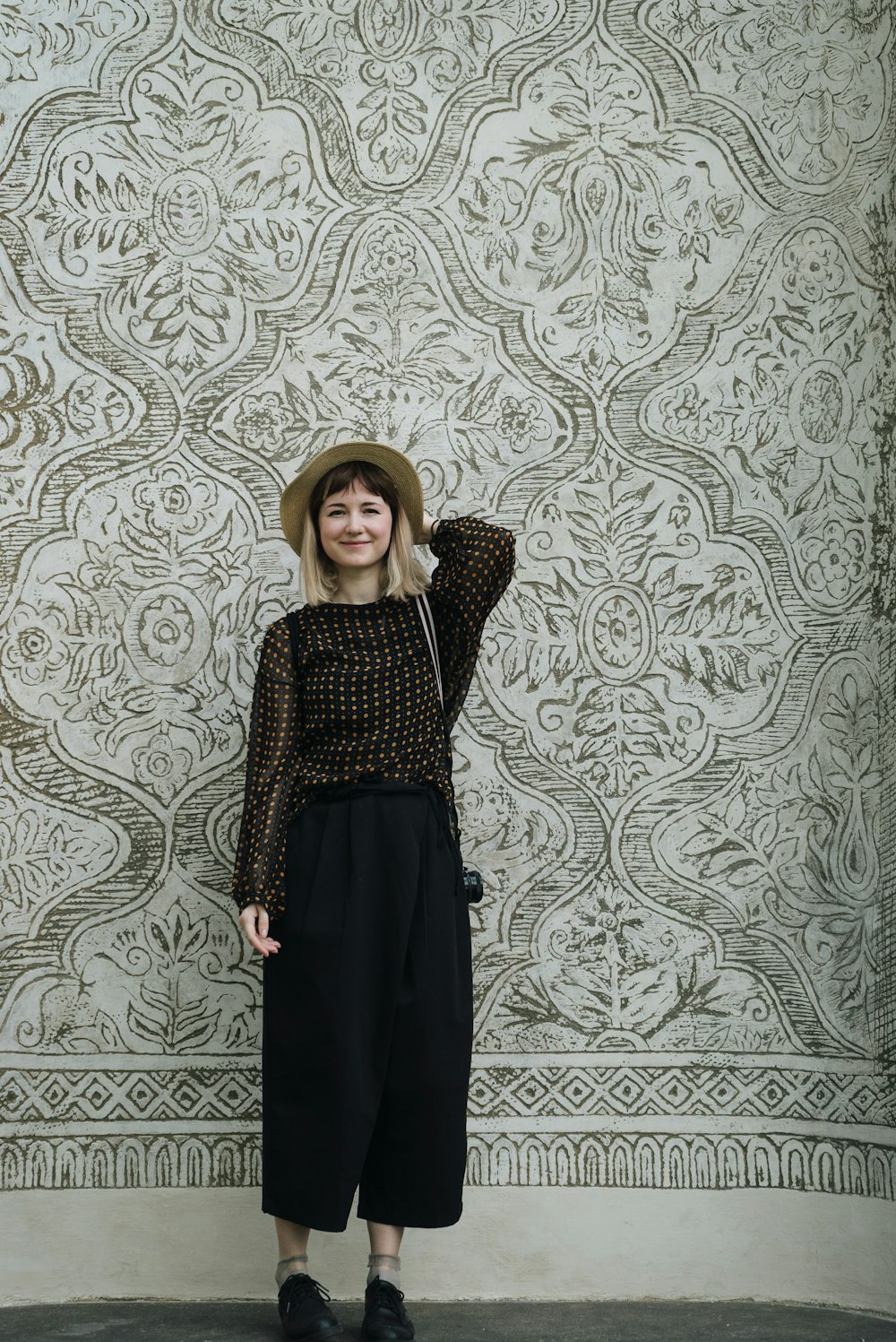 a woman standing in front of a wall wearing a hat