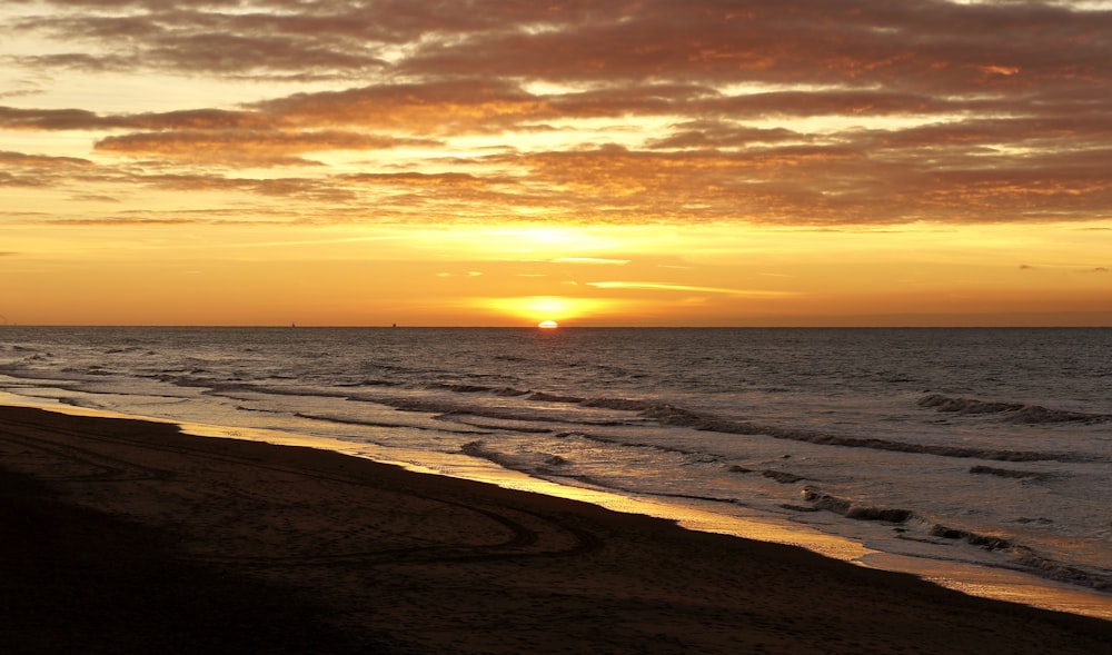 the sun is setting over the ocean on the beach