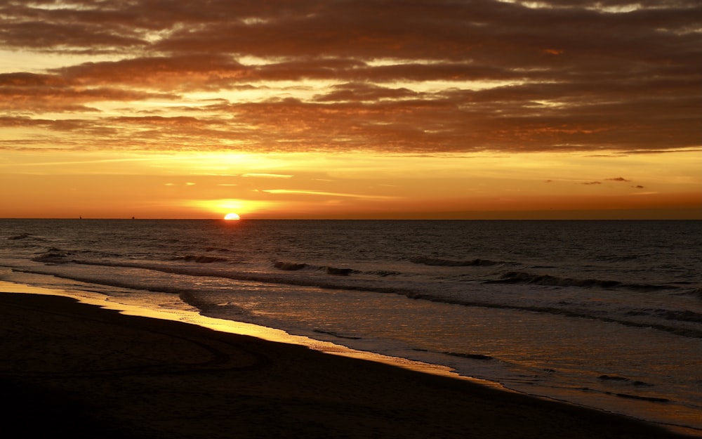 the sun is setting over the ocean on the beach