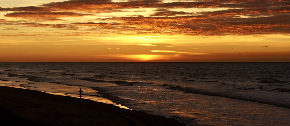 a sunset over the ocean with a person walking on the beach