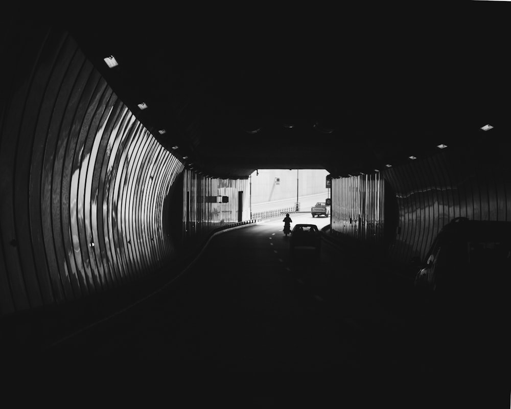 a black and white photo of a person walking in a tunnel