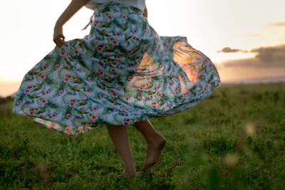 A sunlit open field where a free-spirited girl twirls in a flowing floral dress, barefoot and carefree.