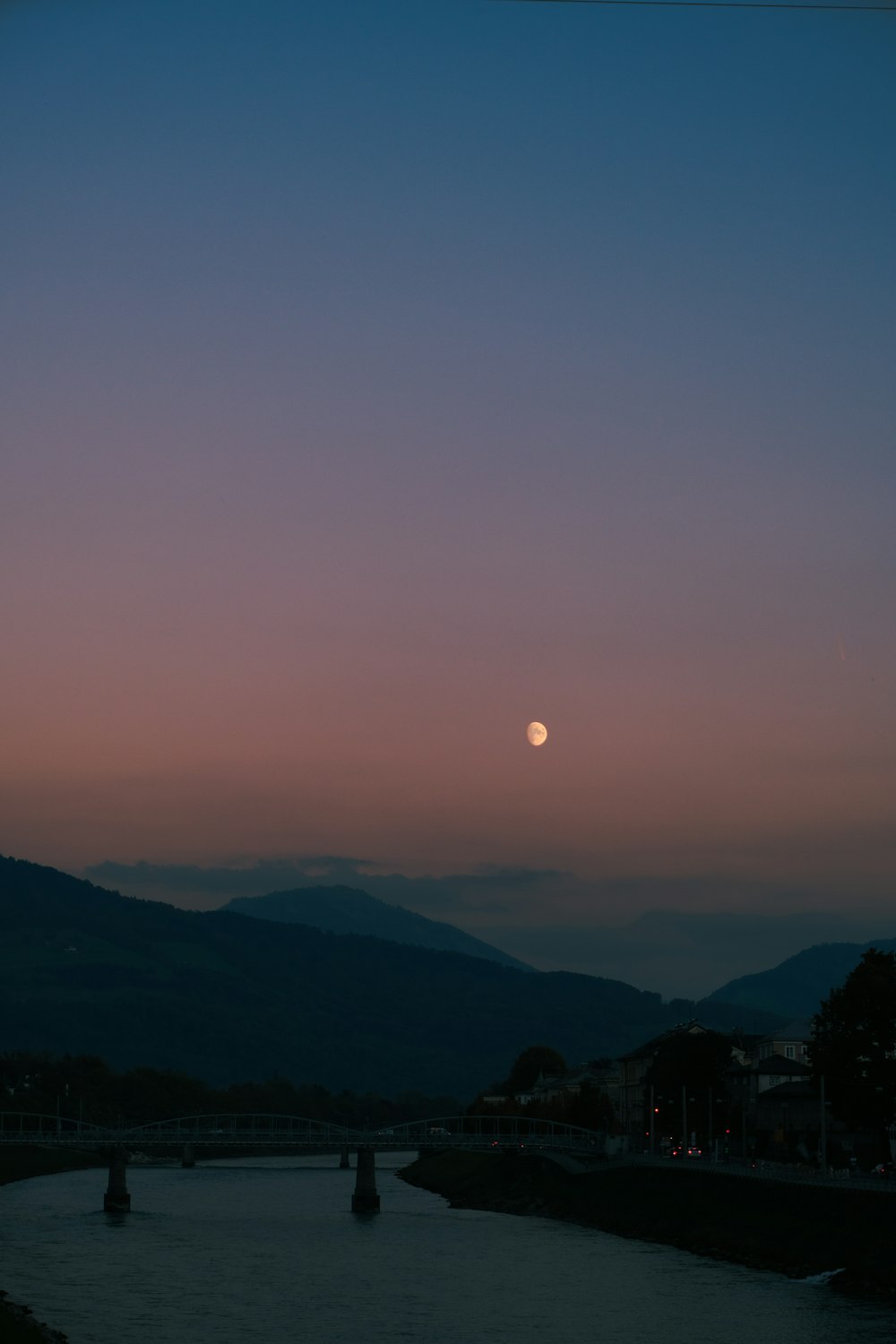 the sun is setting over a river with mountains in the background