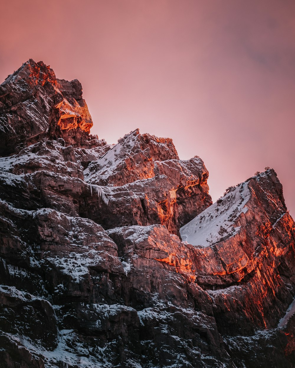 a very tall mountain covered in snow under a pink sky