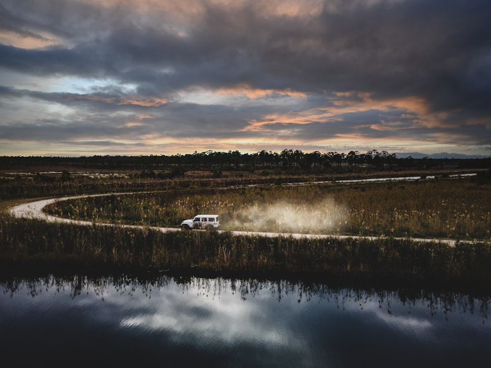 a van driving down a dirt road next to a body of water