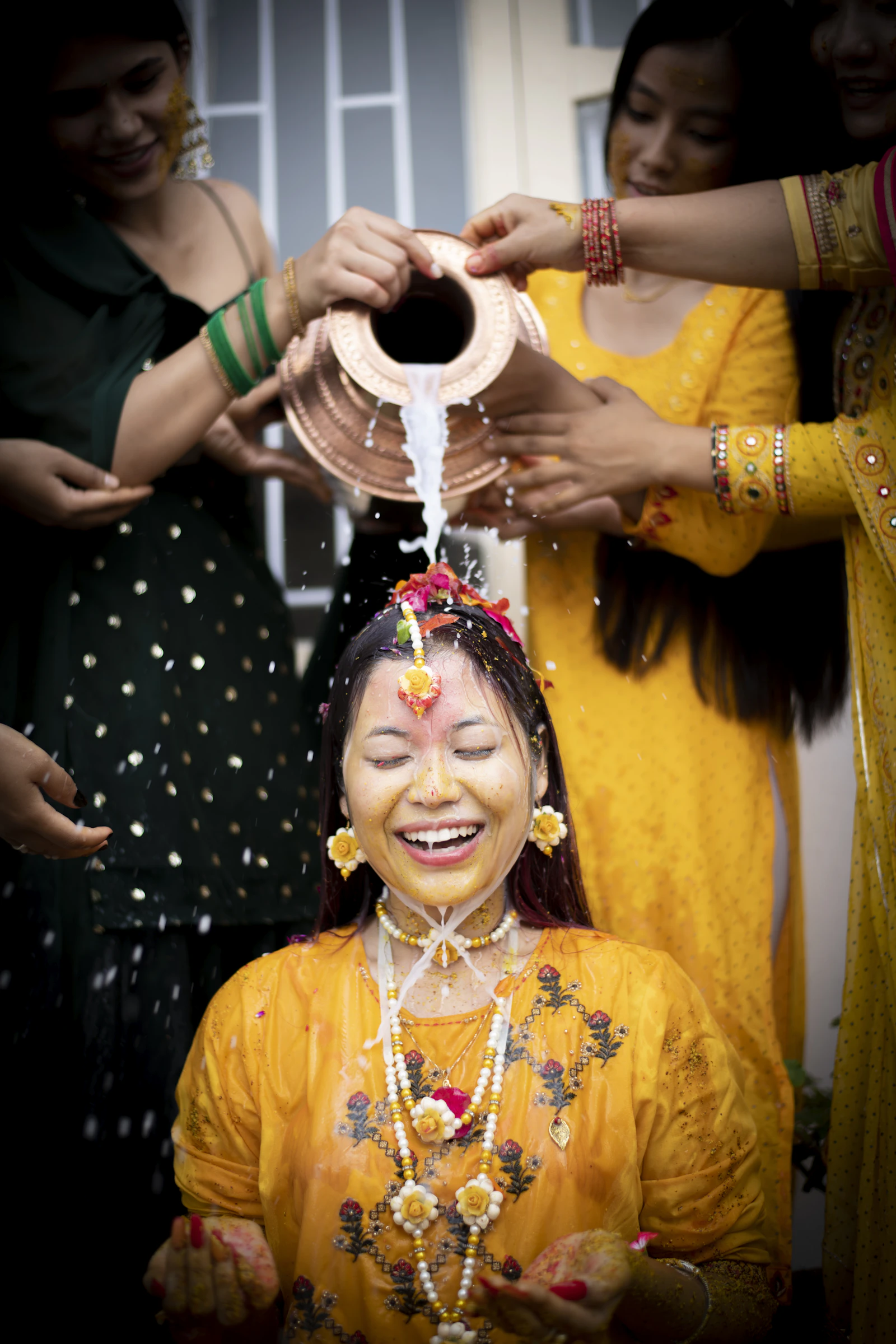 Turmeric paste being applied to a bride by a group of women at a haldi.