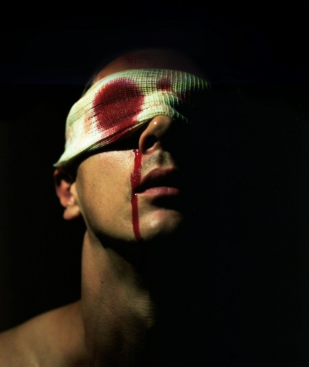Un uomo con una benda sulla testa e una croce rossa dipinta sul viso