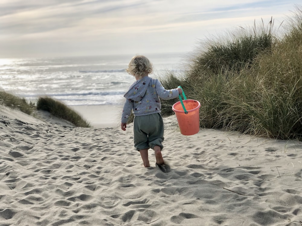 Una bambina che trasporta un secchio e un secchio di sabbia su una spiaggia