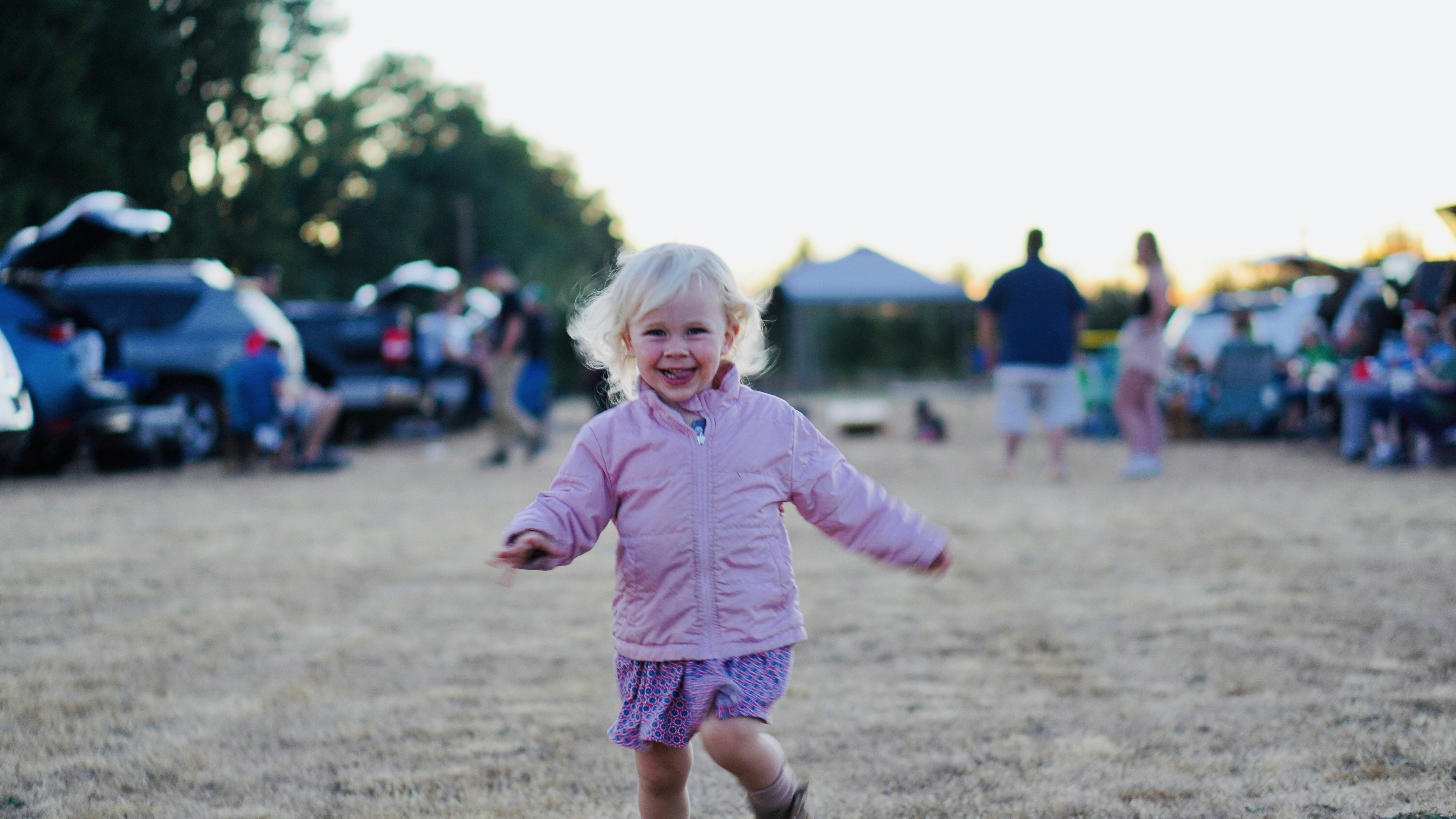 a little girl in a pink jacket is running in a field
