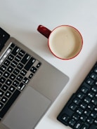 Close-up of hands typing on a keyboard with a red accent coffee mug nearby