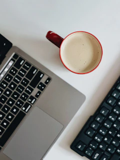 Close-up of hands typing on a modern keyboard with a vibrant coffee mug nearby.