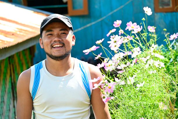 Smiling homeowner standing proudly beside a beautifully landscaped garden with blooming flowers.