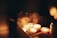 A person appears to be resting near several lit candles, enveloped in warm and soft lighting. The ambient glow creates a serene and intimate setting, emphasizing relaxation.