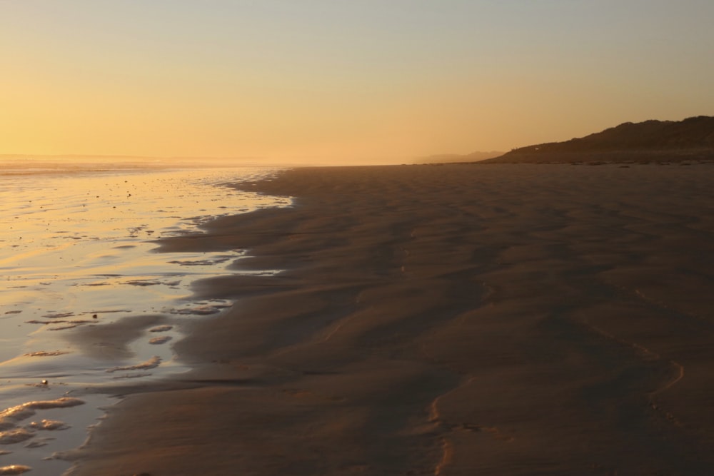 the sun is setting on the beach with footprints in the sand