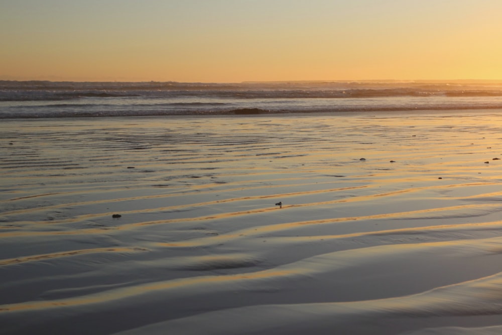 the sun is setting over the ocean and sand