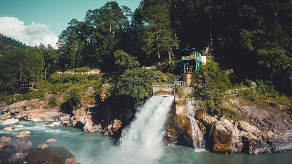 a waterfall with a bridge over it surrounded by trees