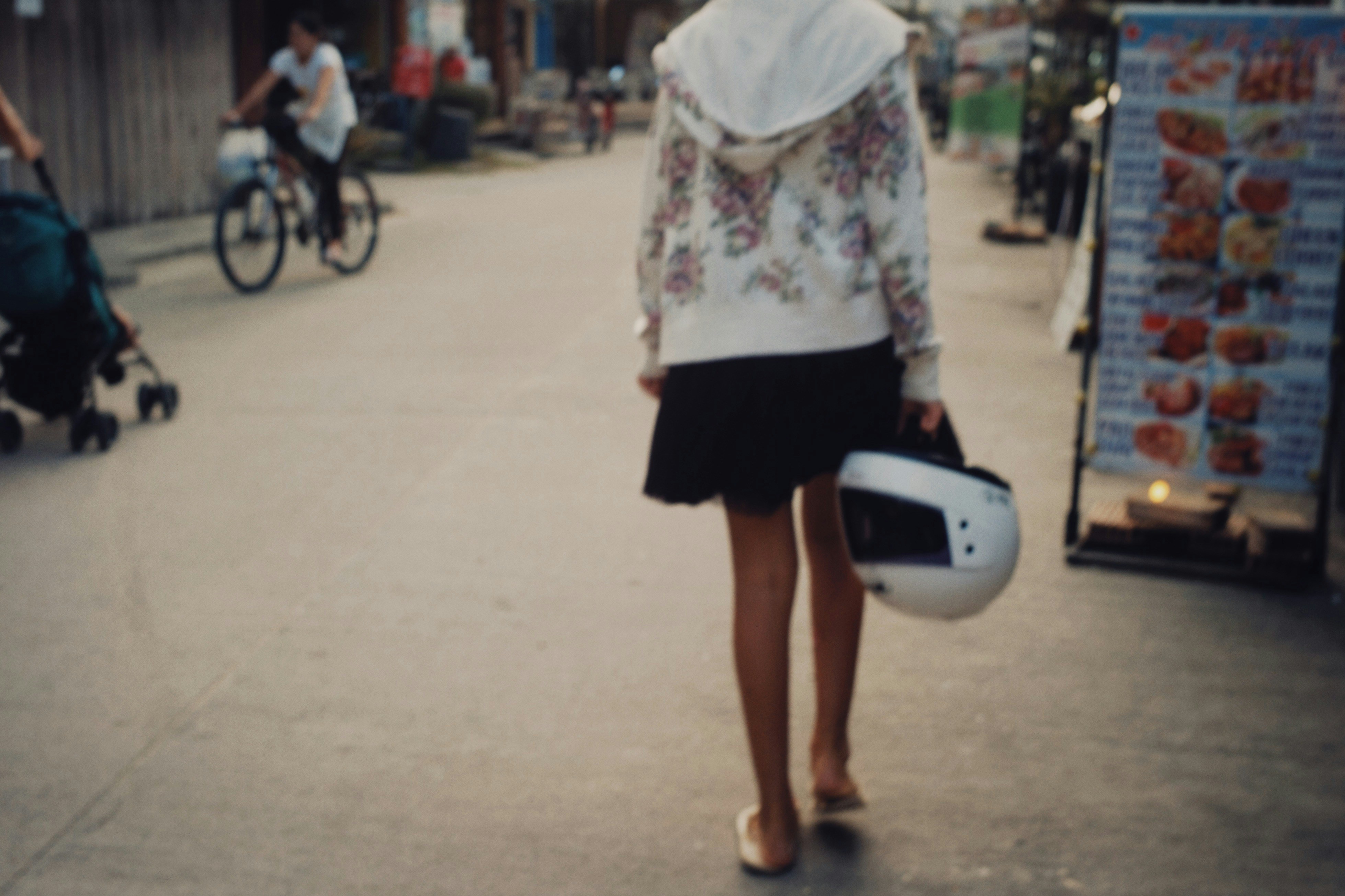 a woman walking down a street holding a helmet