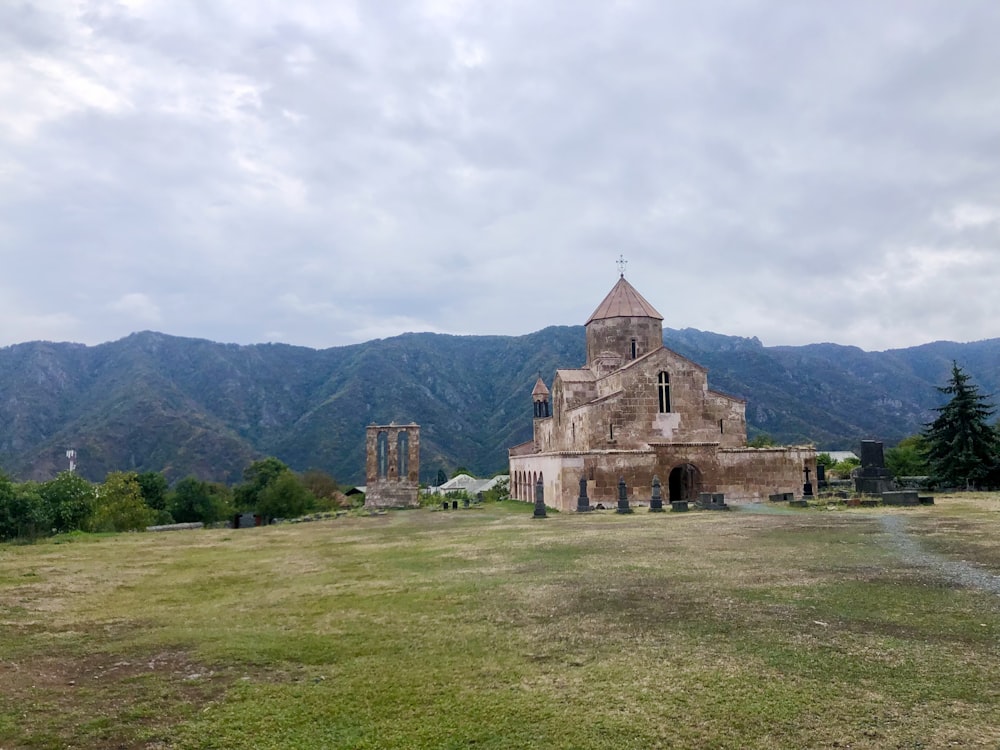 an old church in a field with mountains in the background