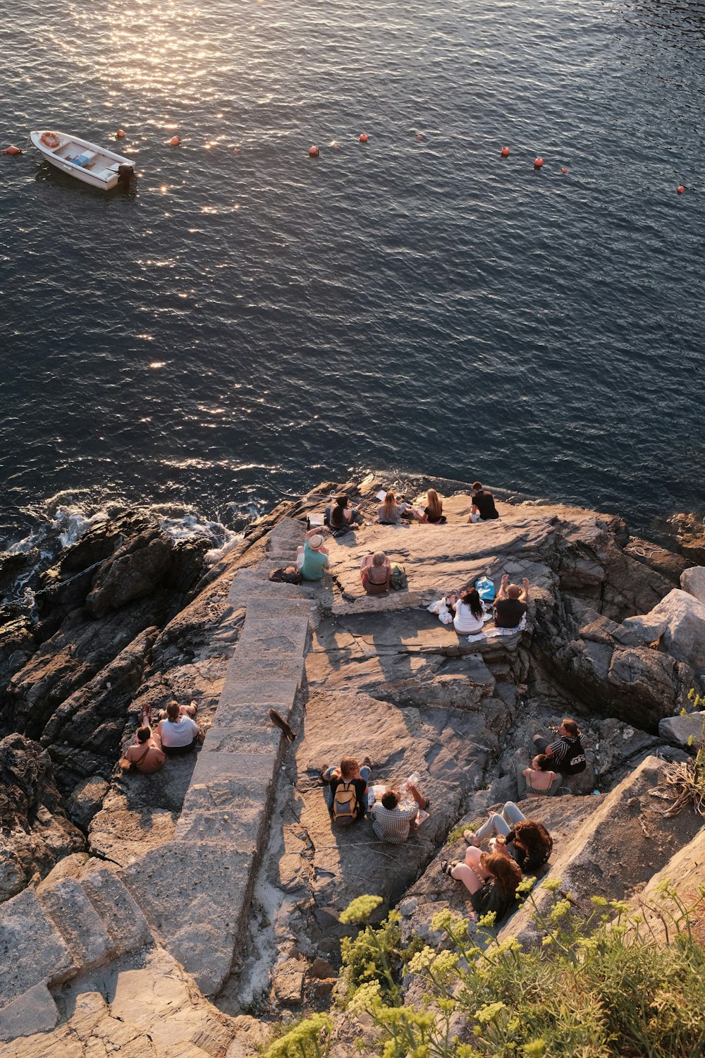 a group of people sitting on top of a cliff next to a body of water