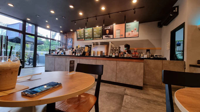 A minimalist modern cafe interior with a focus on a clean counter displaying colorful drinks and desserts.