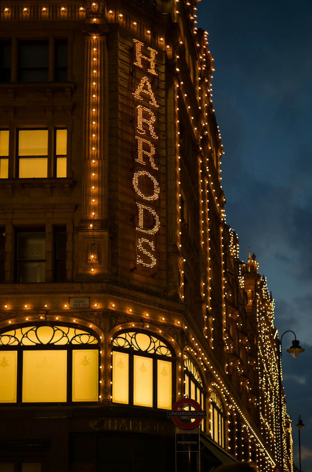 Un bâtiment avec un panneau indiquant que Harrod s’illumine la nuit