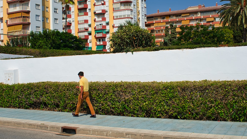 a man walking down a sidewalk next to a hedge