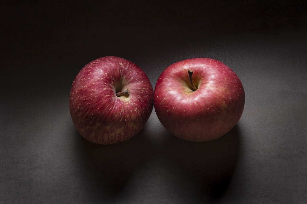 two red apples sitting side by side on a black surface