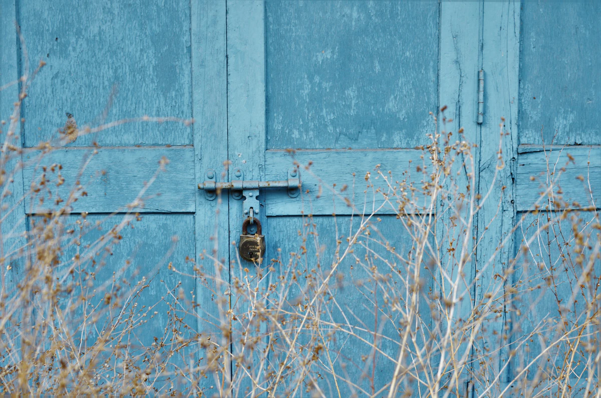 Pintu biru terkunci gembok dengan rumput kering di depannya