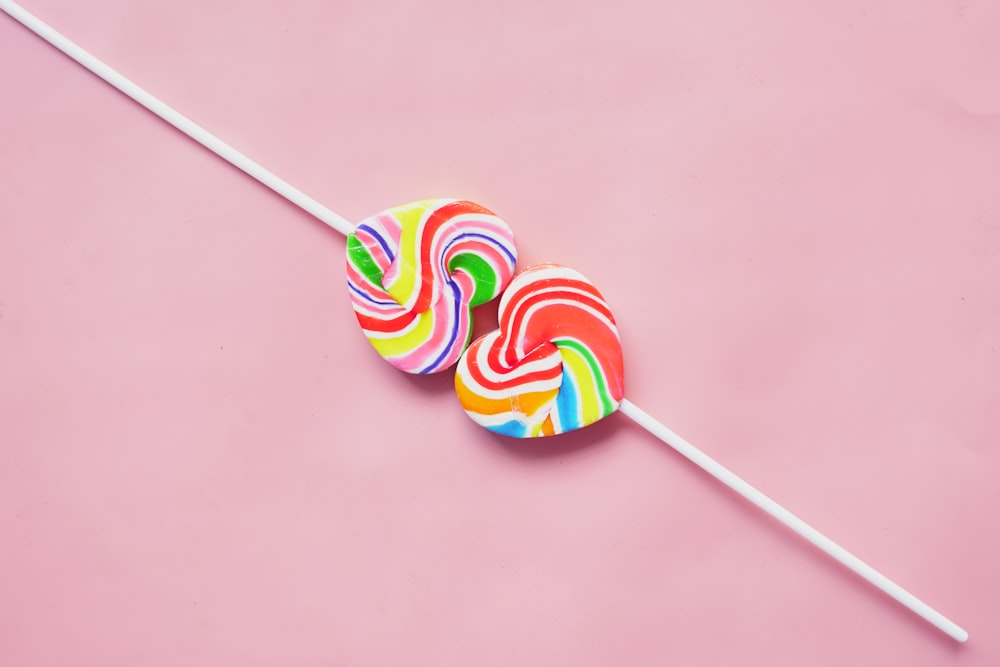 two lollipops sitting on top of a pink surface
