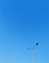 Minimalist black-and-white image of a solar street light standing tall against a clear sky.