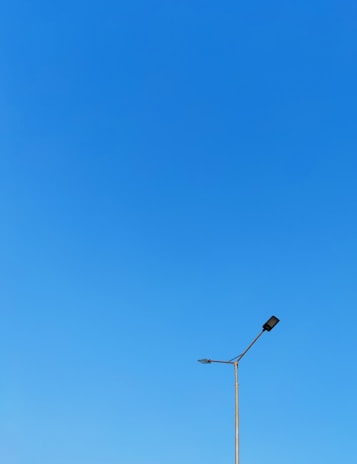Minimalist black-and-white image of a solar street light standing tall against a clear sky.
