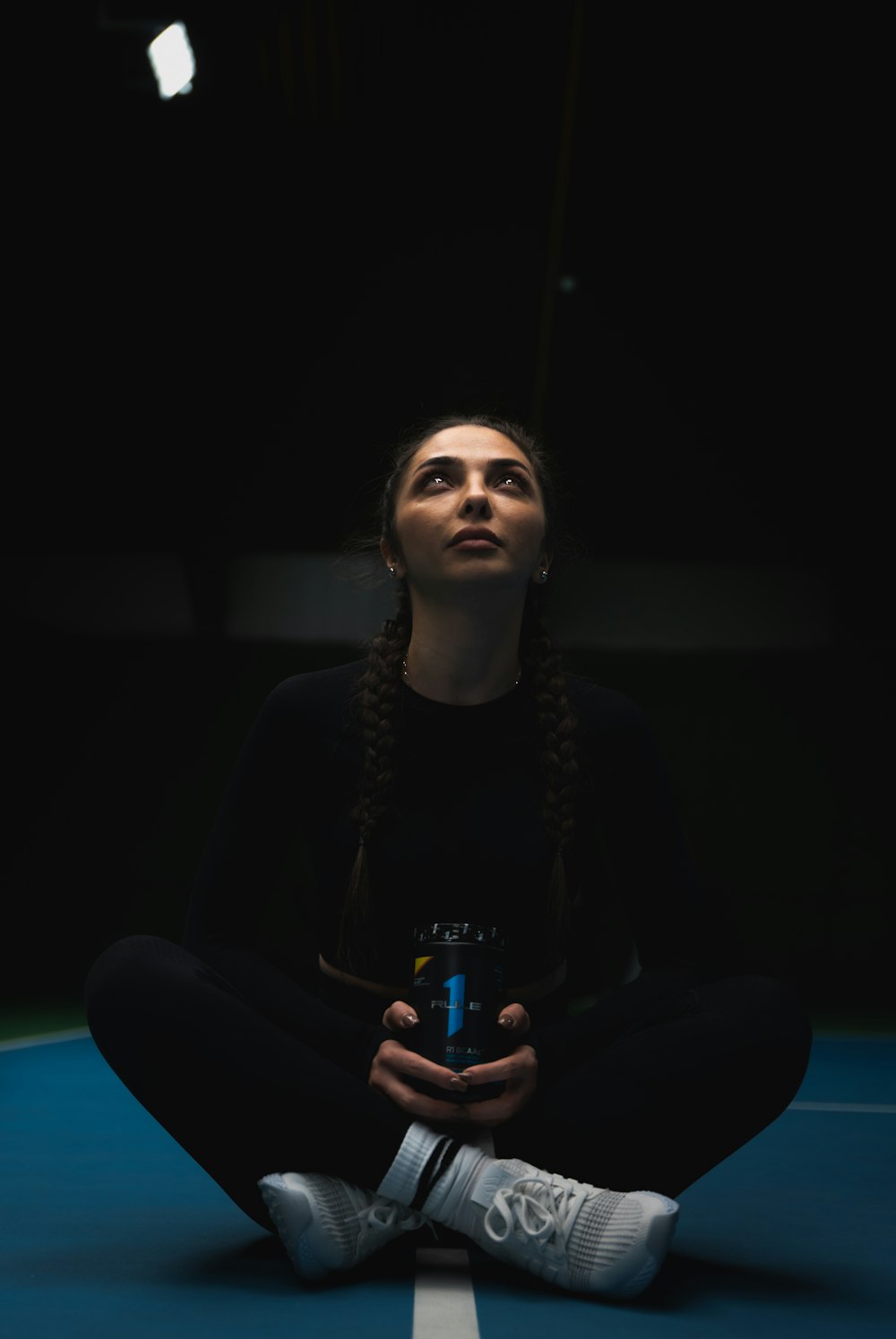 a woman sitting on a tennis court holding a can