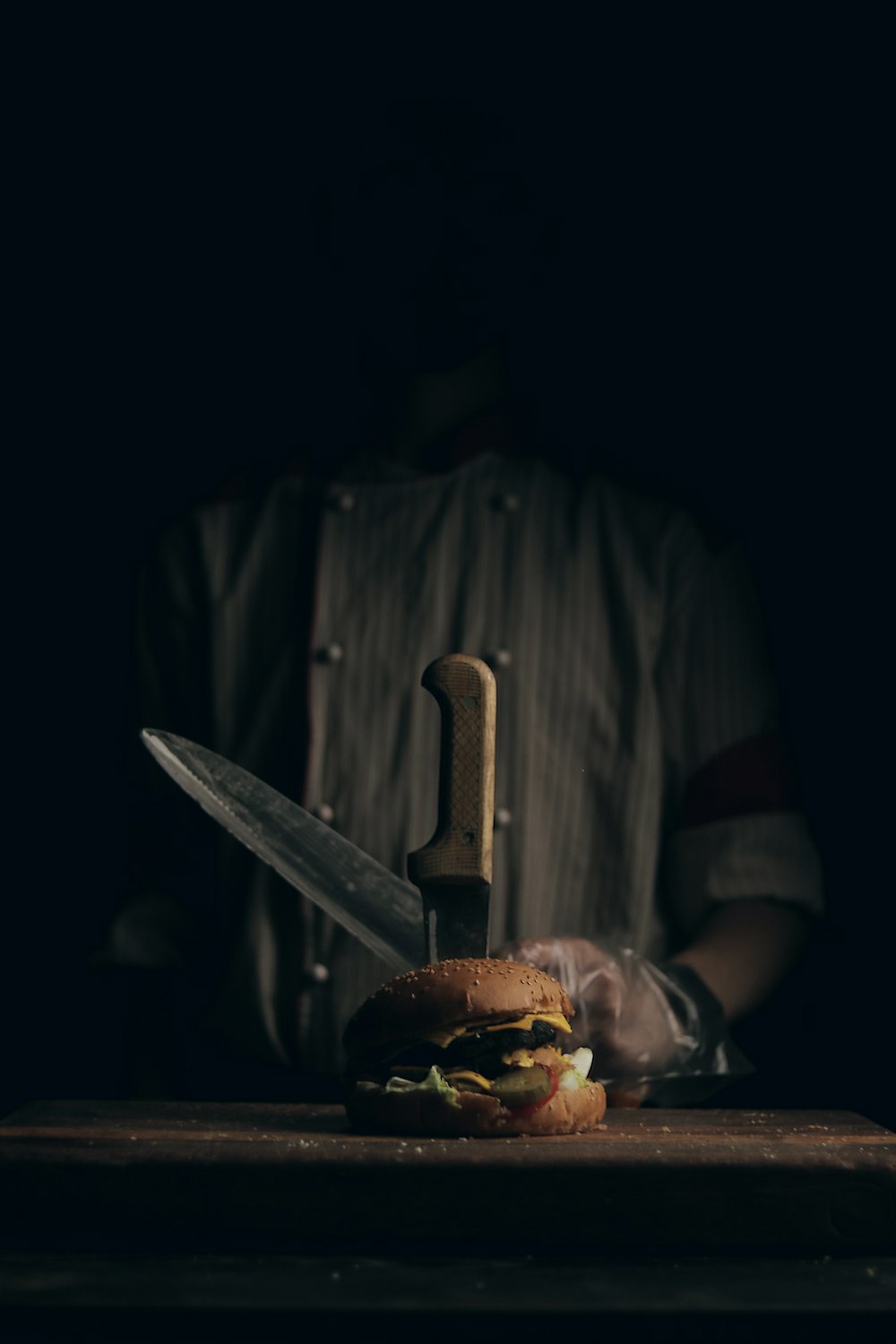 a person holding a knife in front of a hamburger