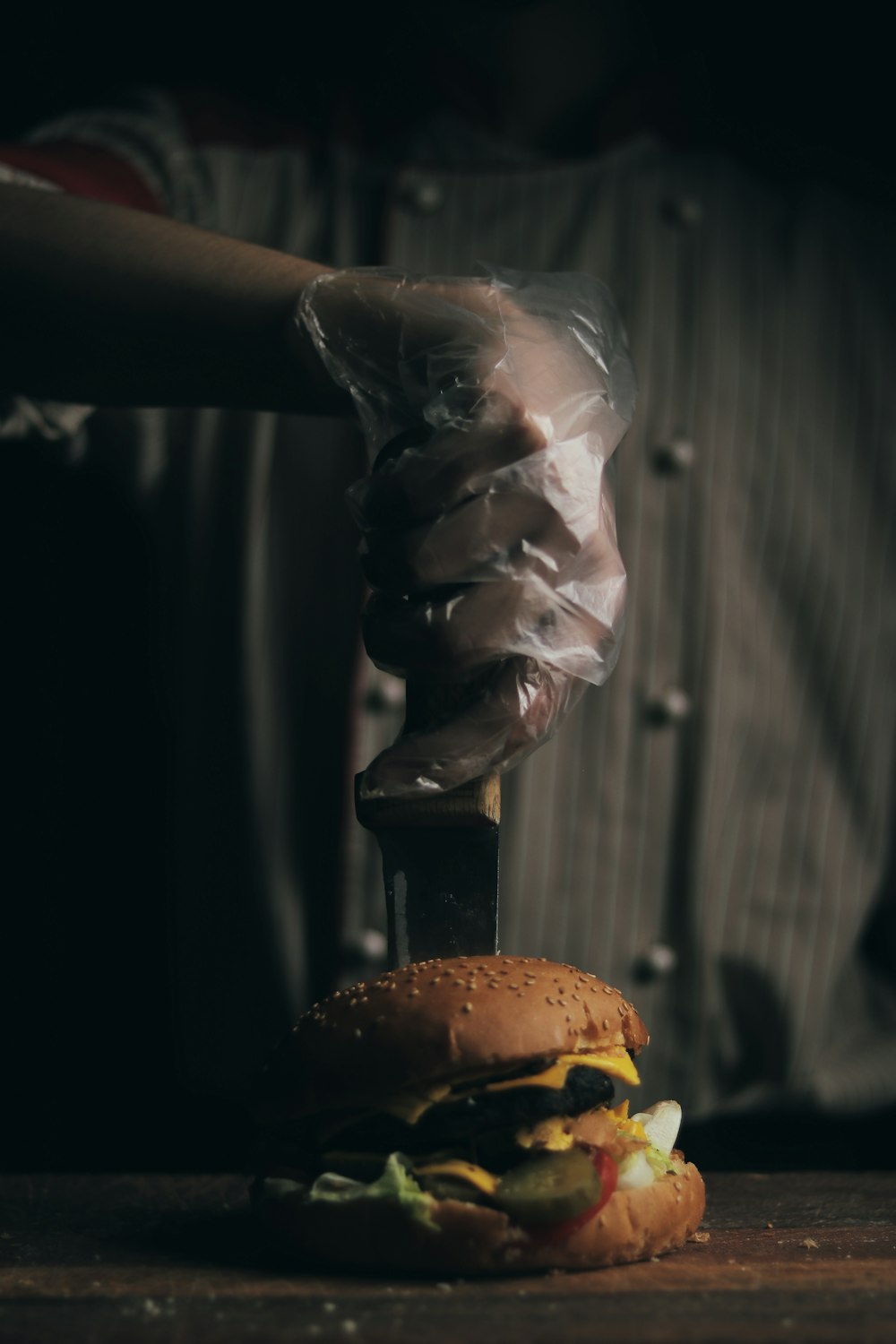a person holding a knife over a hamburger