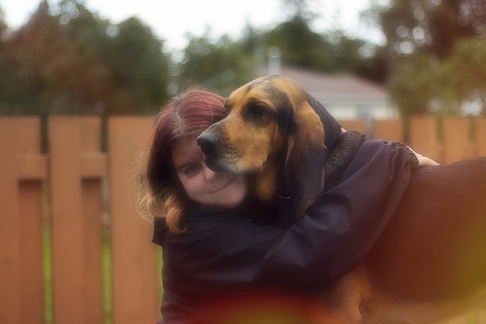 a woman hugging a dog in a fenced in area