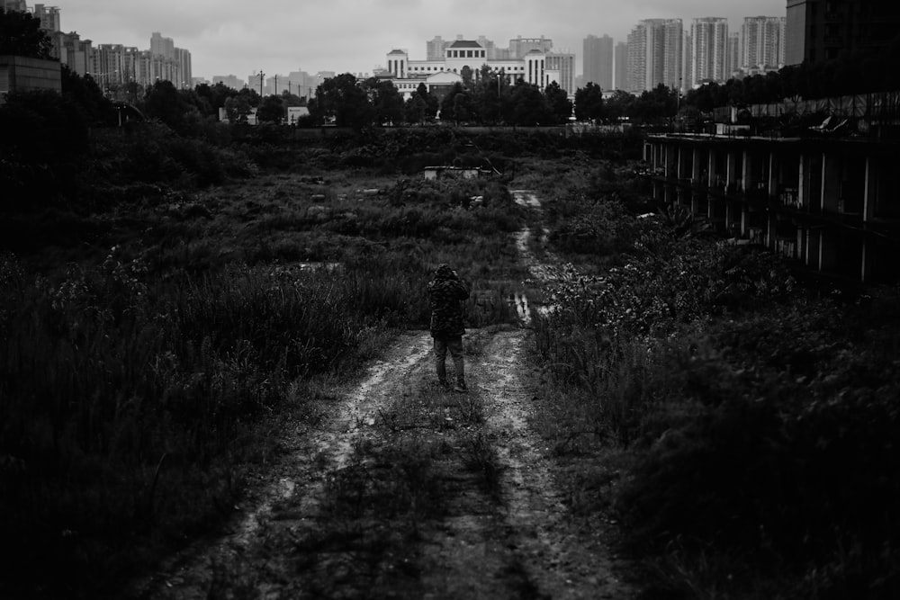 a black and white photo of a person walking down a dirt road