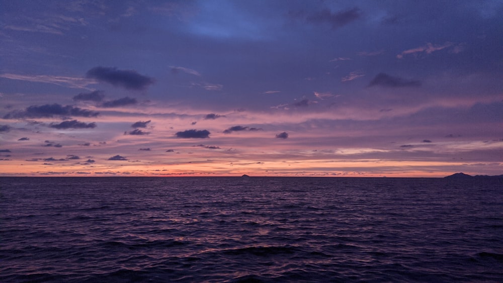 a sunset over the ocean with a small island in the distance