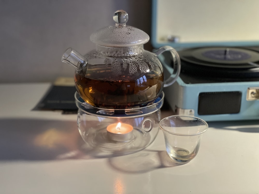 a glass tea pot with a teacup next to it