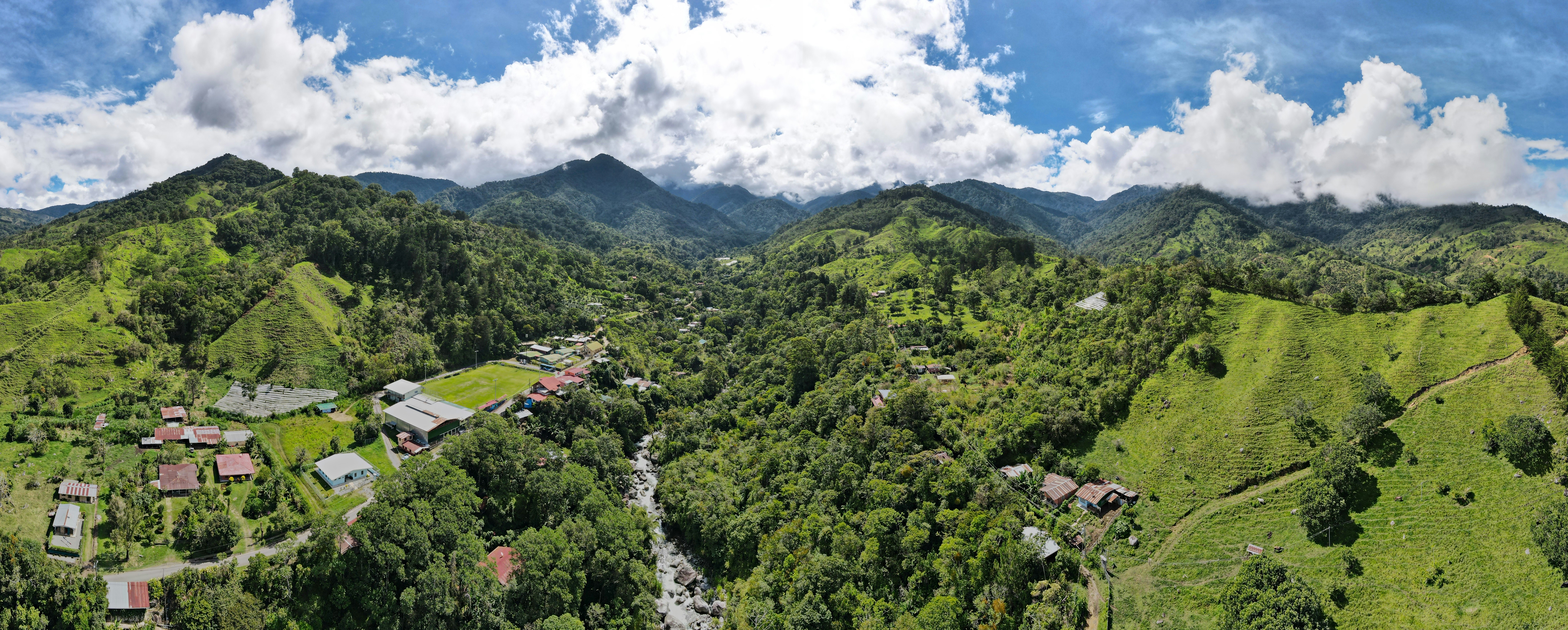 an aerial view of a village surrounded by mountains, An aerial drone panorama of the town of San Gerardo de Rivas and Cerro Chirripó National Park in the background.